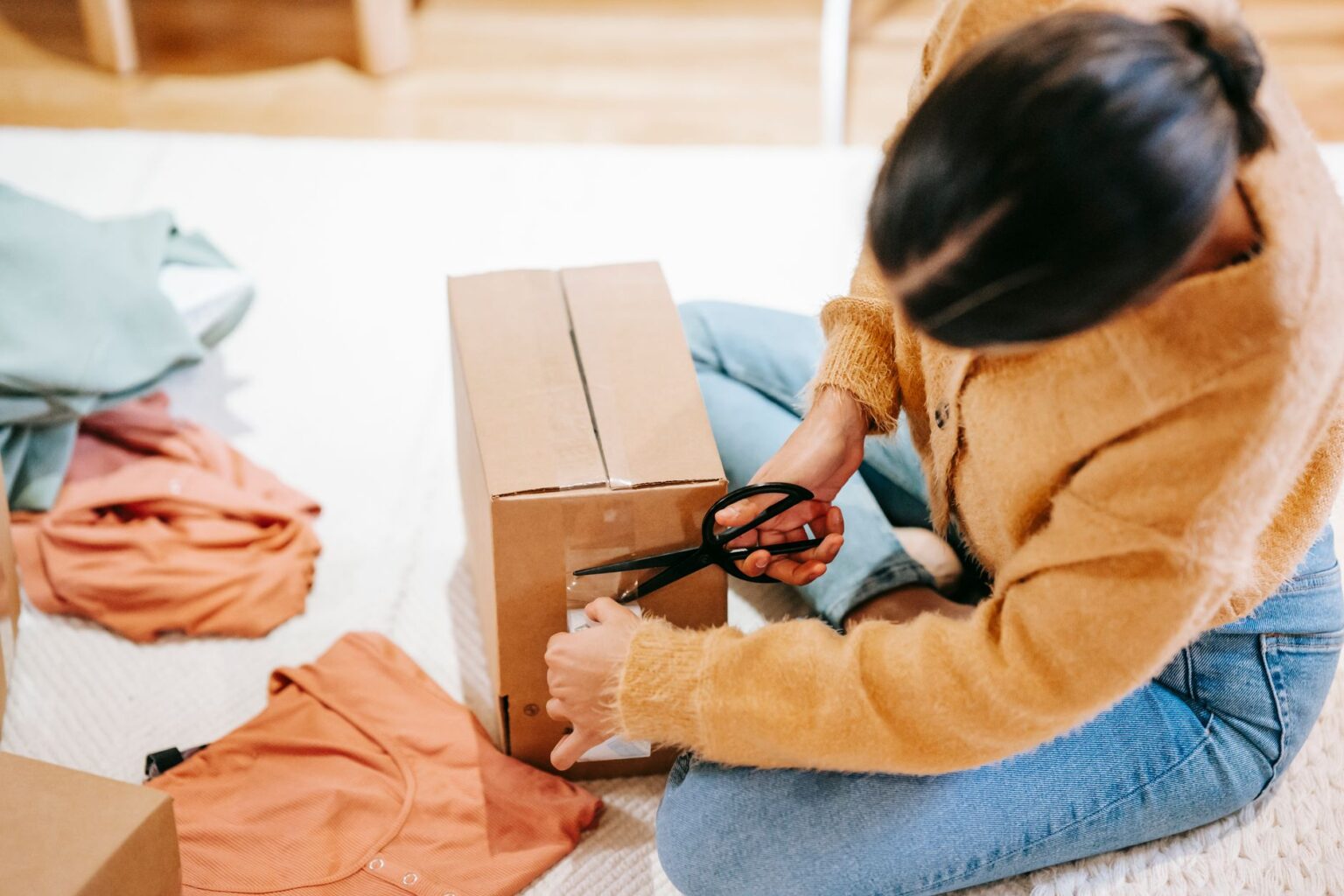 Mulher lacra uma caixa de papelão com roupas ao lado, preparando a devolução de um pedido comprado online