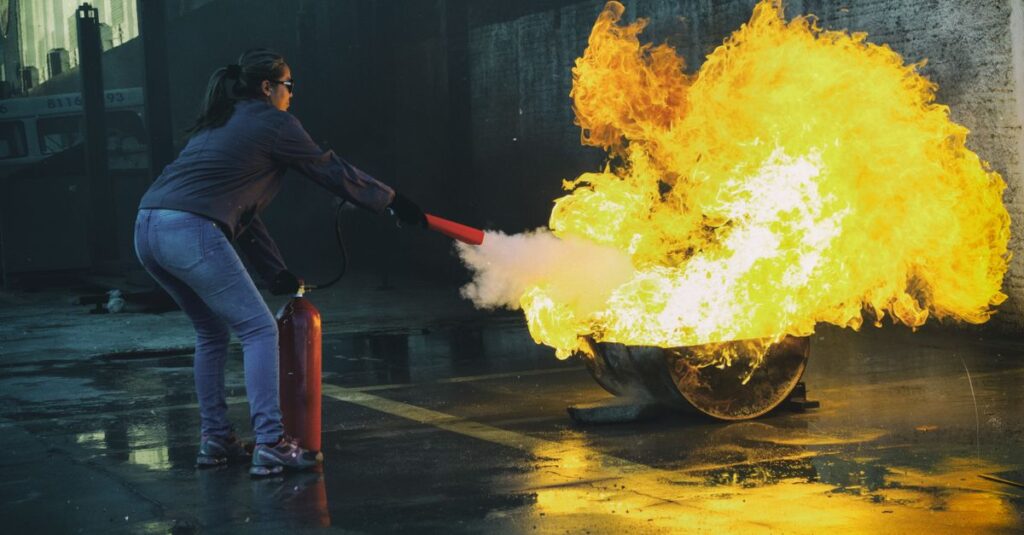 Como Usar um Extintor de Incêndio Corretamente Mulher usando extintor para apagar fogo em um ambiente industrial